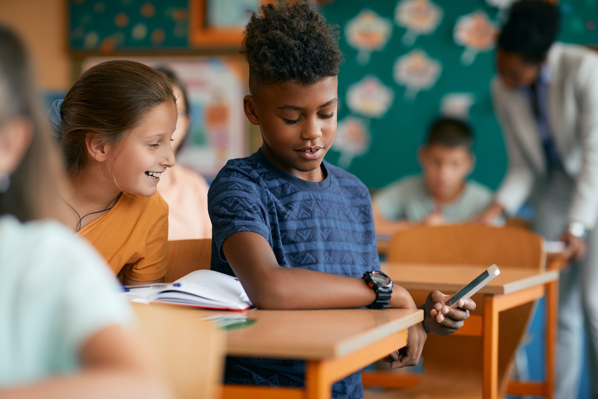 Happy elementary students using mobile phone during a class at school.