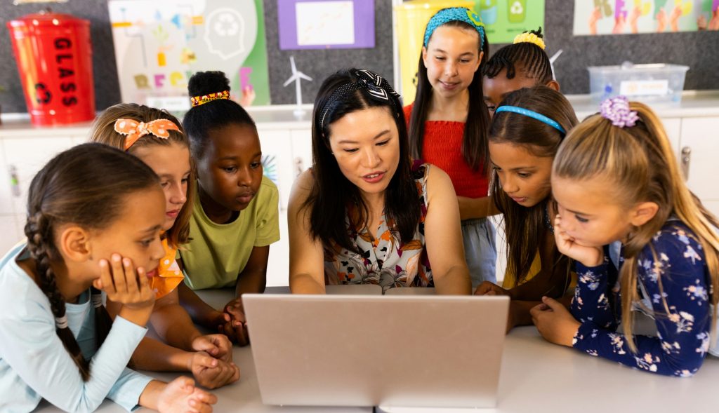 Diverse female teacher with laptop and elementary schoolgirls in class