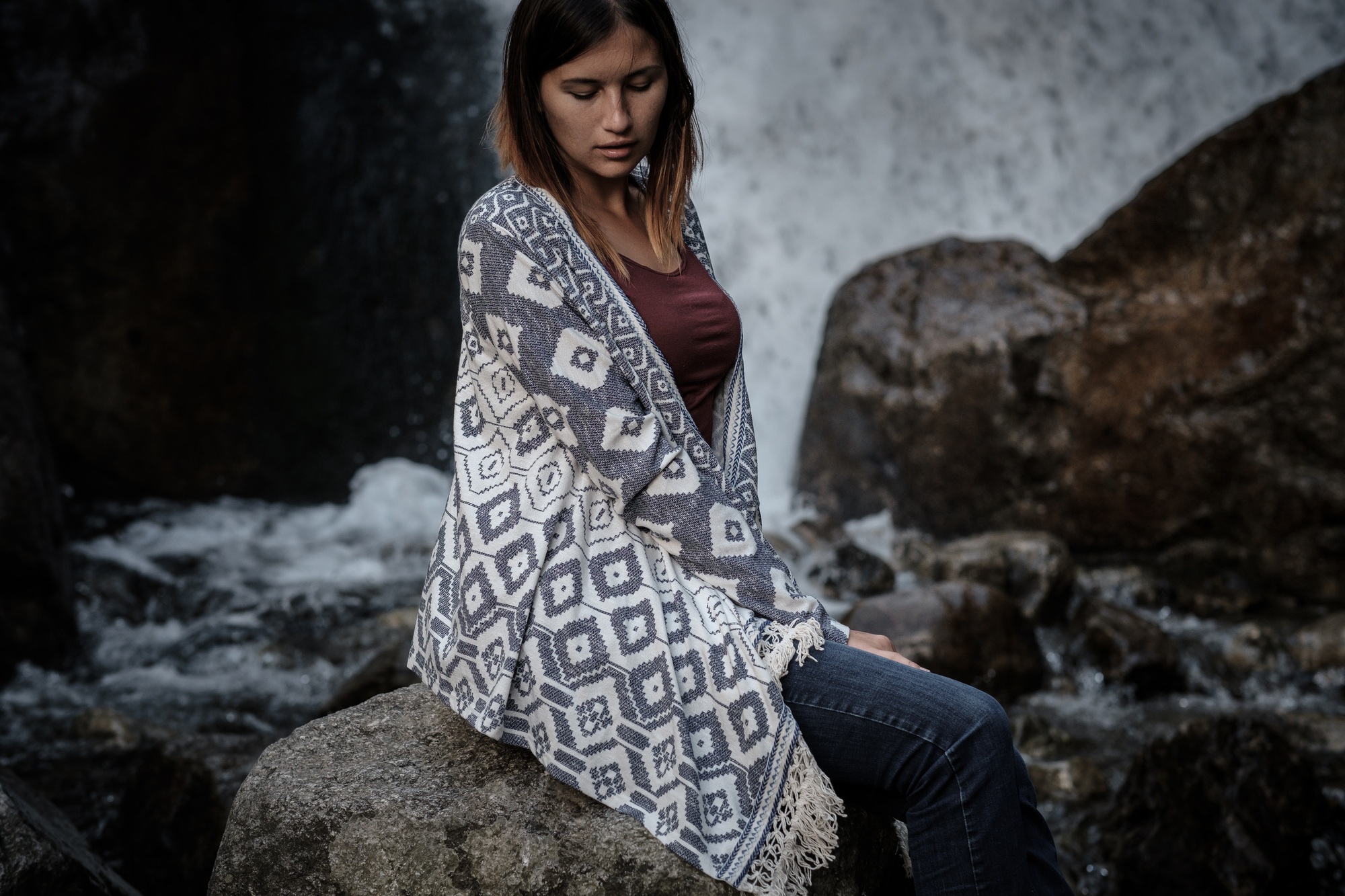 Boho woman wearing hat and poncho standing by the waterfall and looking at it